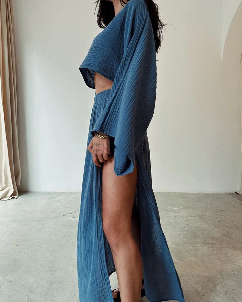 Model draagt linnen katoenen tweedelige dames set voor de zomer, vakantie outfit linnen rok met hoge taille en sexy split bij de benen aan beide kanten en linnen katoenen top met lange wijde mouwen en dunne losse stof blauw