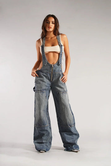 model draagt sexy overall van spijkerstof denim jumpsuit met open buik blote buik en wijde pijp losse broek overall