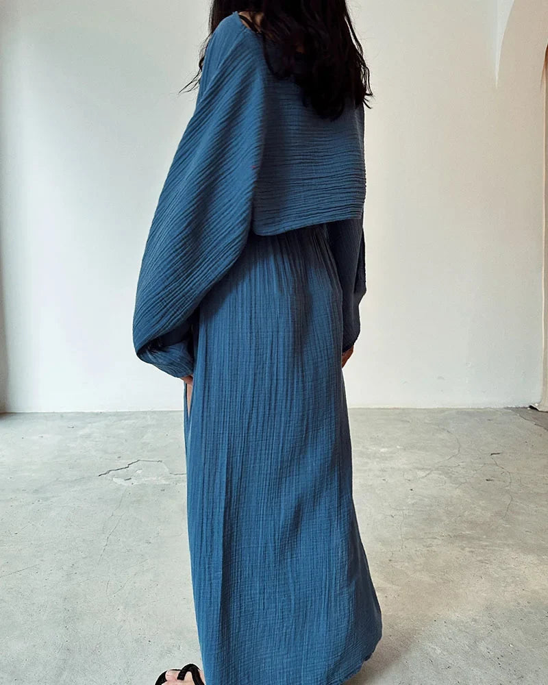 Model draagt linnen katoenen tweedelige dames set voor de zomer, vakantie outfit linnen rok met hoge taille en sexy split bij de benen aan beide kanten en linnen katoenen top met lange wijde mouwen en dunne losse stof blauw